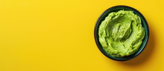 Obraz premium Avocado dip presented in a bowl atop a yellow backdrop with ample copy space image It is a nutritious spread made from avocados seen from a top down perspective
