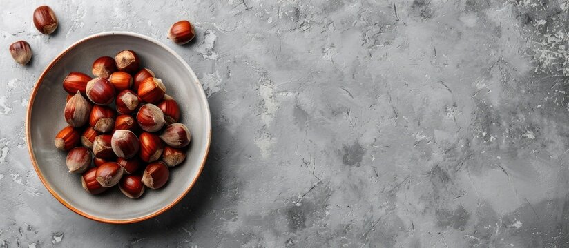 Top view of a bowl containing fresh edible sweet chestnuts on a grey table with ample copy space for text in the image