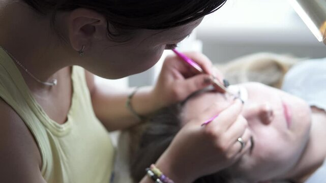 A master performs an eyelash extension procedure in a beauty salon. Beauty industry.