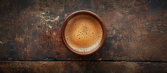 Top view of a frothy coffee in a brown cup on a wooden surface with space for adding more images. Copy space image. Place for adding text and design