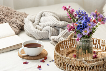 Cup of tea, a bouquet of wildflowers, book and knitted element.