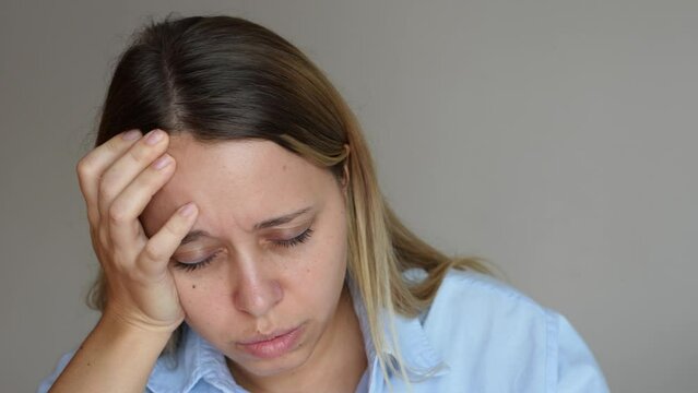 A young caucasian blonde woman feeling dizzy holding her head with hand on grey background. Dizziness, vertigo, fatigue, low blood pressure, anemia, headache, migraine, exhaustion, emotional breakdown