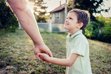 Rearview shot of a little boy holding his father's hand while walking together outdoors. Beautiful boy looking at father while holding hands.