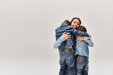 A young Asian mother and her little sons, wearing denim clothes, hugging each other in front of a...
