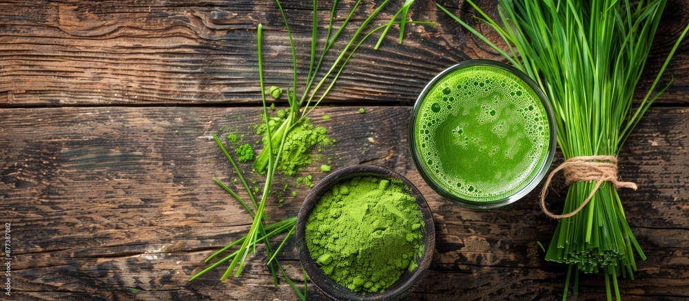 Poster view from above of a glass of fresh wheatgrass juice and powder on a wooden surface with a blank spa