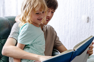 Smiling Boy Reading Book to Little Sister on Couch
