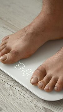 A Caucasian barefoot obese man weighs himself on an electronic scale. Close-up of a man's feet. Vertical video. 