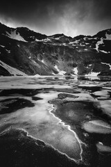 Photo en noir et blanc d'un lac de montagne dans les Pyrénées Andorranes avec encore des restes de glace à la surface du lac
