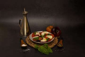 A colorful and appetizing plate of classic Caprese salad on a black background, accompanied by an oil jug and some ingredients