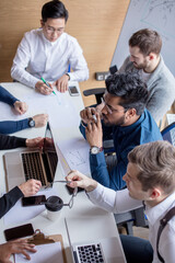 Mixed race team of experienced marketers gather around a table to do research and implement new ideas. High angle view of multi-ethnic business people discussing in board room meeting