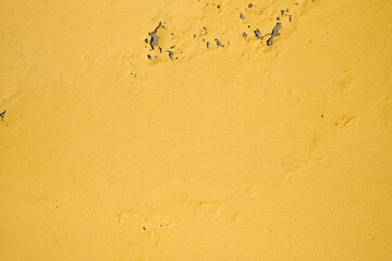 Yellow peeling paint on the old rough concrete wall, weathered rough painted wall with patterns of cracks and peeling