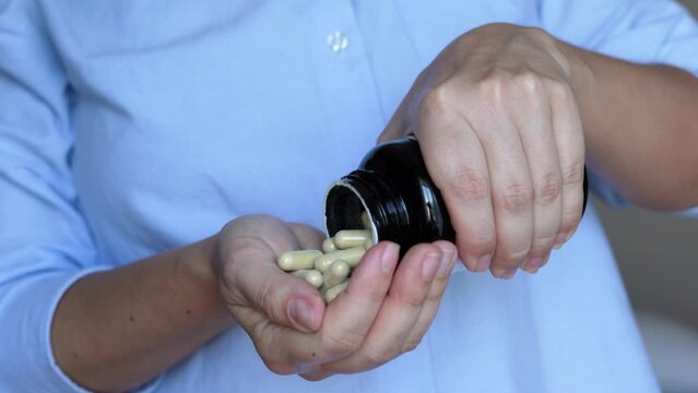 Cropped shot of a young woman in a blue shirt taking a medicine. The girl taking vitamins by pouring pills from a jar on her hand. Treatment of the disease. Dietary supplements