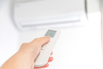 Fototapeta premium Hand Holding Remote Control Adjusting Air Conditioner