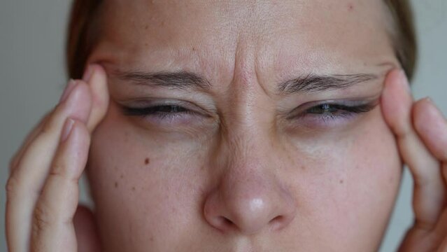 Young caucasian woman with poor eyesight squints pulling eyelids to the sides with hands on a grey background. Vision focus	