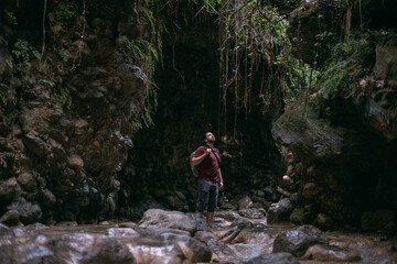Obraz premium A young male tourist walks along a shallow tropical mountain river among the rocks.