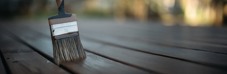 Close-up, a man's hand in a work glove with a painting brush paints boards outdoors.