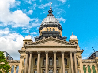 Obraz premium Front Views of the Illinois State Capitol Building in Springfield, IL, USA. Cloudy blue skies overhead. Scaffolding and construction equipment with ongoing construction on the building.