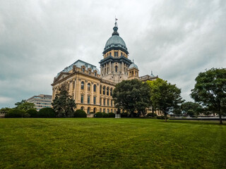 Obraz premium Long view of the Illinois State Capitol Building in Springfield, IL, USA. Cloudy overcast skies overhead. Springtime scene with a lush green lawn and full trees.