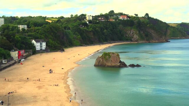 Tenby, Pembrokeshire, Wales: July 3rd 2024: 4K video, footage of families enjoying the evening sunshine on the golden sands of Tenby's north beach. The tide is up and water warm enough for paddling.