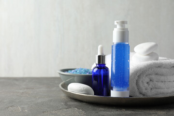 Spa composition. Cosmetic products, terry towel and sea salt on gray table against light background, space for text