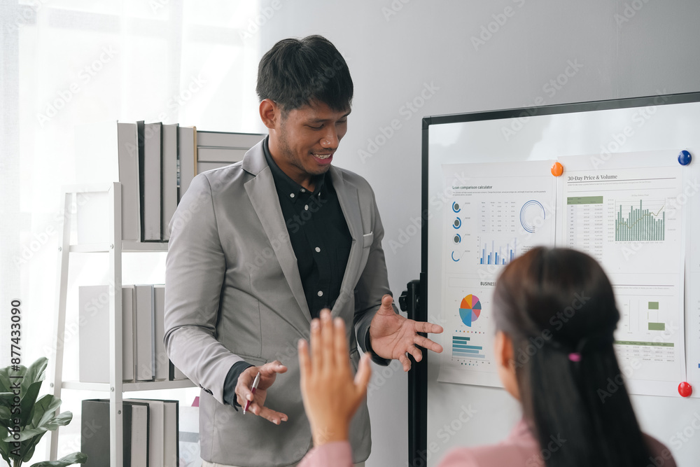 Poster businessman explaining strategy to colleague while pointing at charts on a whiteboard and colleague 