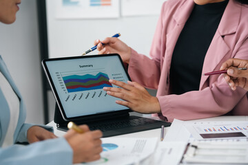 Businesswomen working together, pointing at tablet screen and analyzing financial data using digital tablet during meeting in modern office