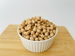 Raw dry chickpea in small ceramic bowl with wooden board on white background. Traditional ingredient for cooking hummus. Middle Eastern and Mediterranean cuisine. Selected focused