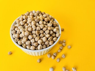 Raw dry chickpea in small ceramic bowl on yellow background. Traditional ingredient for cooking hummus. Middle Eastern and Mediterranean cuisine. Selected focused