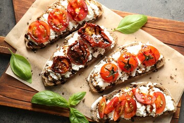 Delicious ricotta bruschettas with sun dried tomatoes, sauce and basil on grey textured table, top view