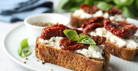 Delicious ricotta bruschettas with sun dried tomatoes, basil and milled pepper on light table, closeup