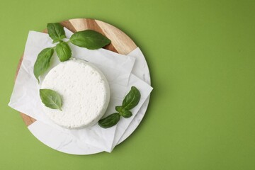 Fresh ricotta (cream cheese) and basil on green table, top view. Space for text