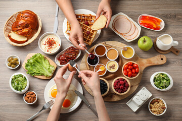 People having breakfast at wooden table, top view