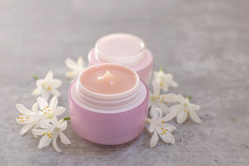 Cream in jars and beautiful jasmine flowers on grey table, closeup