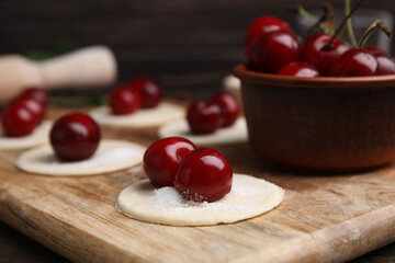 Process of making dumplings (varenyky) with cherries. Raw dough and ingredients on wooden table, closeup