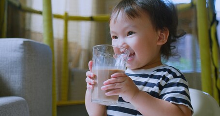 Adorable Cute Toddler enjoying Drinking Chocolate Milk in a Glass at Home, Capturing a Sweet and Innocent Moment of Childhood