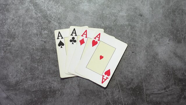 Man's hand placing four cards from a deck with a poker of aces on a textured table