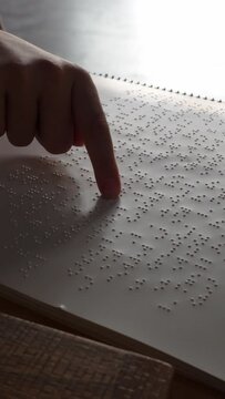 Finger of a girl reading a book in the language of the blind: braille. Vertical video
