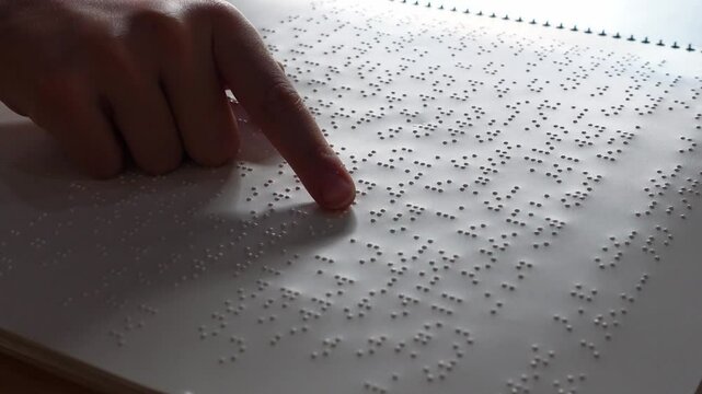 Finger of a girl reading a page from a braille notebook in the language of the blind: braille
