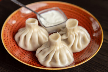 Georgian boiled khinkali. Three khinkali with sauce on plate. Soft focus