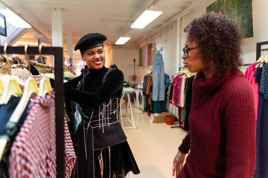 Customers shopping in modern clothing store, retail sales associate assists client