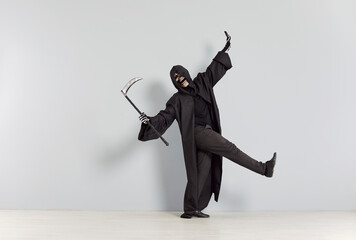 Happy funny man in grim reaper death costume holding scythe wearing black cloak with hood and...