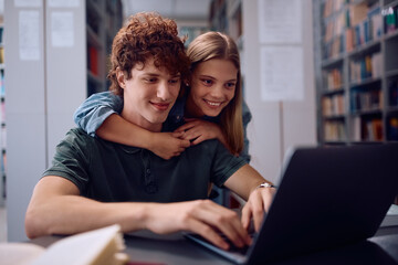 Happy college couple using laptop while learning in library.