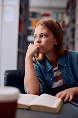 Thoughtful female student learning in library and looking away.