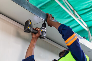 african american man using a power drill overhead on a ceiling