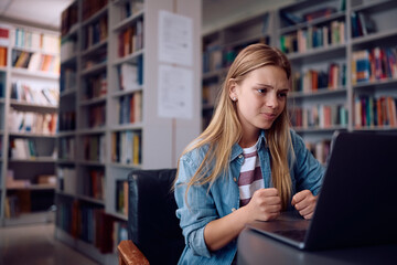 Female student feeling disappointed with exam results while using laptop in library.