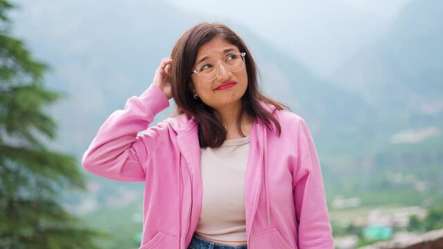 4K Portrait of forgetful Indian girl scratching head in confusion and looking upwards. Forgetful teenager girl student. She is unsure about answer, having doubts, difficult career choice