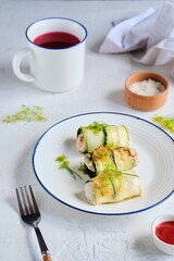 Rolls made of zucchini and chicken breast on a white plate on a light concrete background. Zucchini recipes.