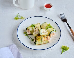 Rolls made of zucchini and chicken breast on a white plate on a light concrete background. Zucchini recipes.