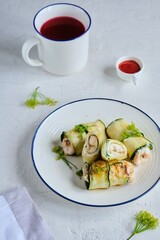 Rolls made of zucchini and chicken breast on a white plate on a light concrete background. Zucchini recipes.