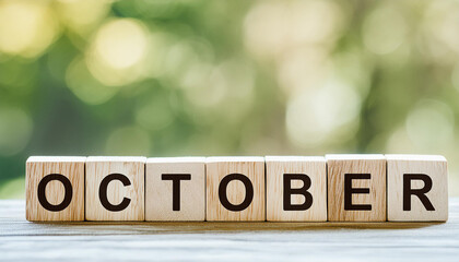 Wooden cubes with text OCTOBER on wooden table with natural green backdrop. Autumn season. Close-up